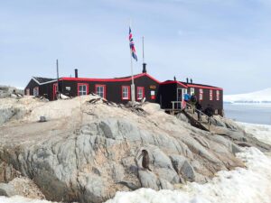 People engaged in research near a building on rocky terrain with penguins in the foreground, in Antarctica, specifically South Georgia
